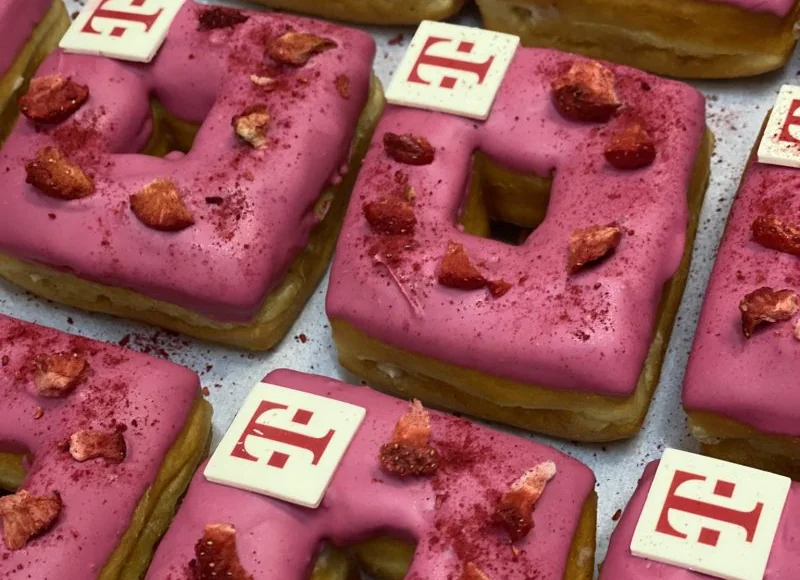 Square donuts with magenta glaze and branded white chocolate toppers on a tray