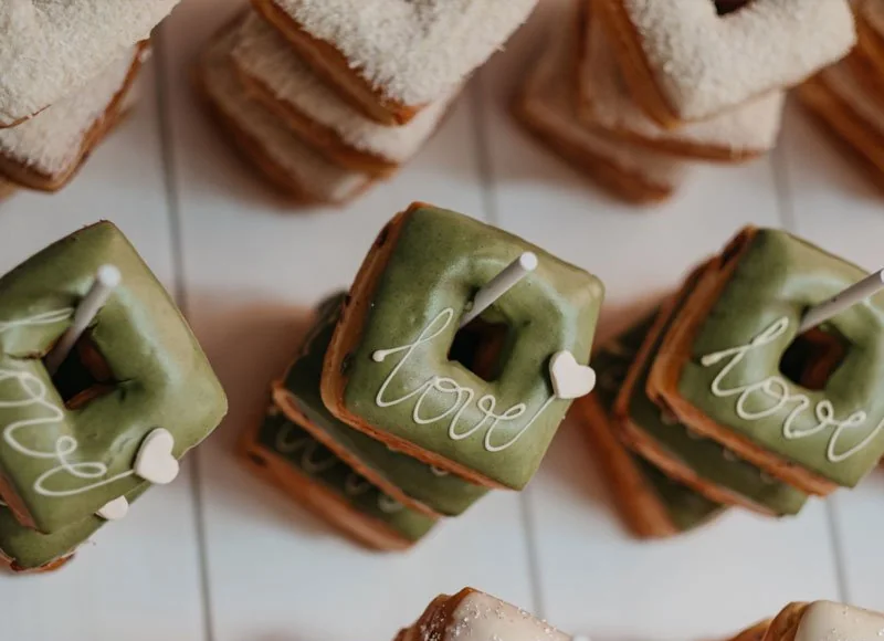 Green frosted square donuts with white lettering on a tiled table at a wedding