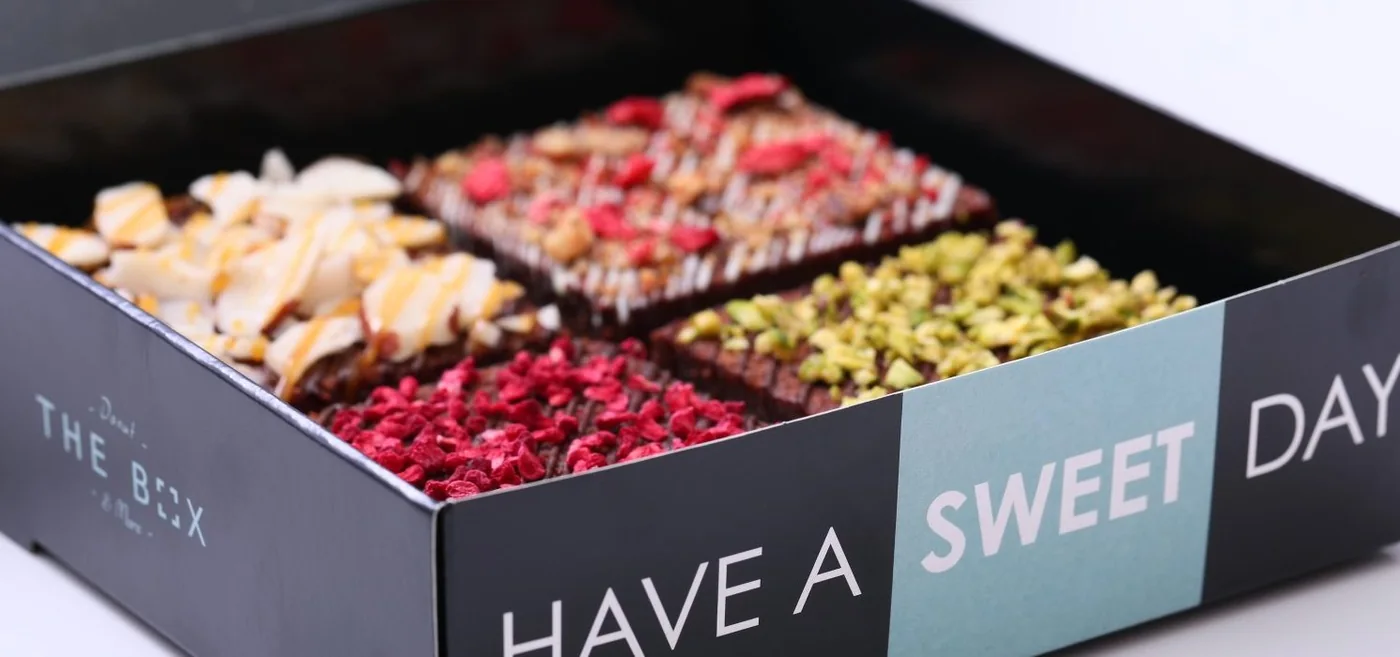 Open THE BOX gift box with four filled square donuts topped with almond, raspberry, pistachio and dried fruit