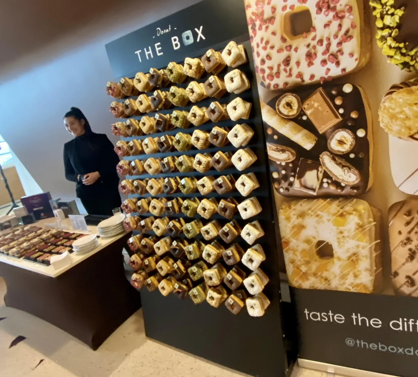 The Box donut wall at an event: rows of square donuts on a branded display next to a table