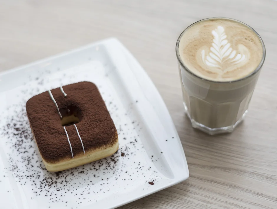 Cocoa-dusted square donut on a plate next to a latte